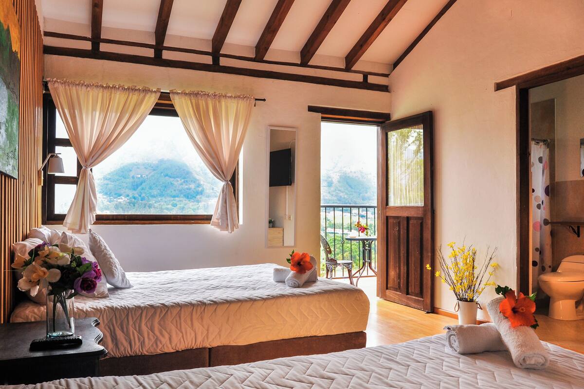 Une chambre d  ’hôtel avec deux lits, un balcon offrant une vue sur les montagnes, et une salle de bain avec des toilettes et une douche.