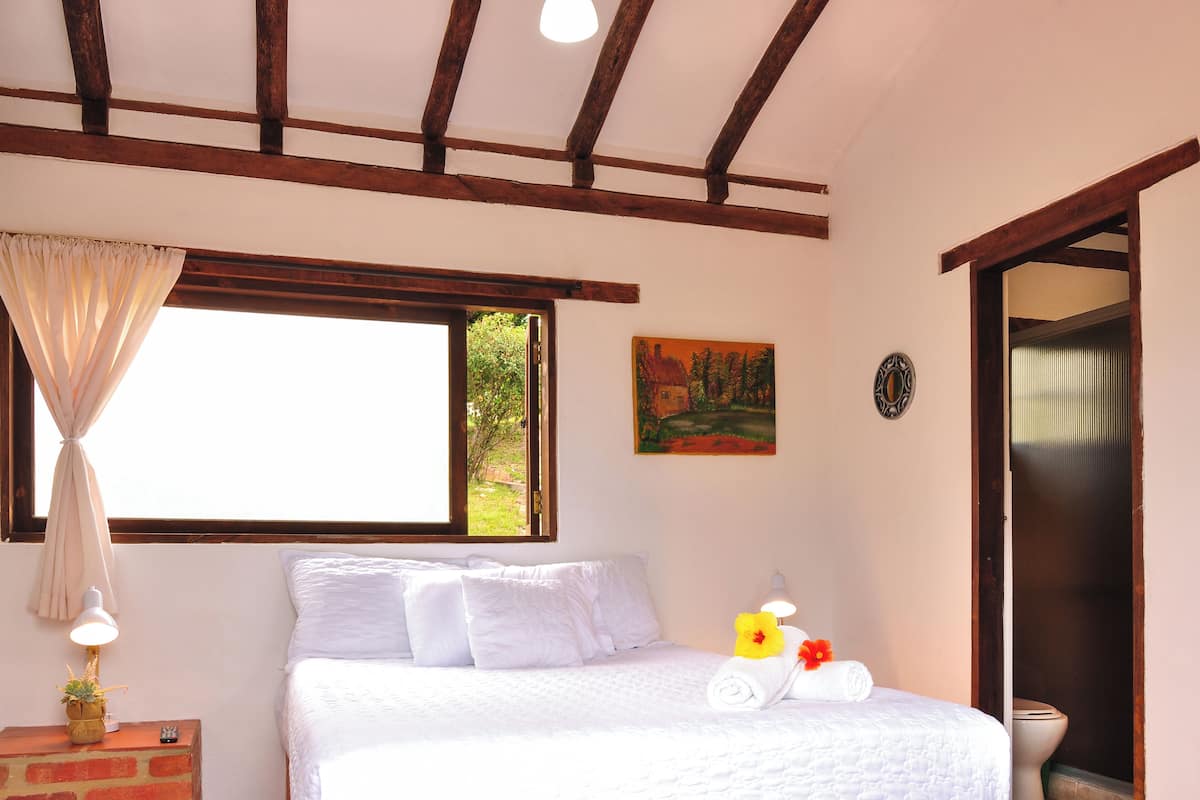 Une chambre à coucher avec un lit, une table de chevet, une fenêtre avec des rideaux, un tableau et une porte.