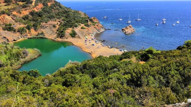 Paisaje costero con playa, mar azul cristalino y barcos.