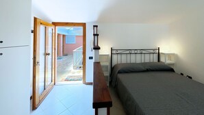 Un dormitorio con una cama, mesitas de noche, un banco y una puerta que da a un balcón.