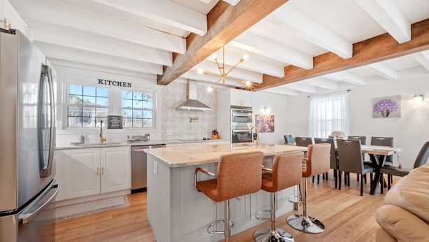Una cocina moderna con armarios blancos, una isla grande con taburetes y un comedor con mesa y sillas de madera.