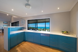 Une cuisine moderne dotée d’une grande fenêtre, d’un plancher en bois et de meubles de rangement bleus.