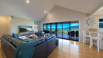 A modern living room with a large sofa, a flat-screen TV, and a view of the outdoors.