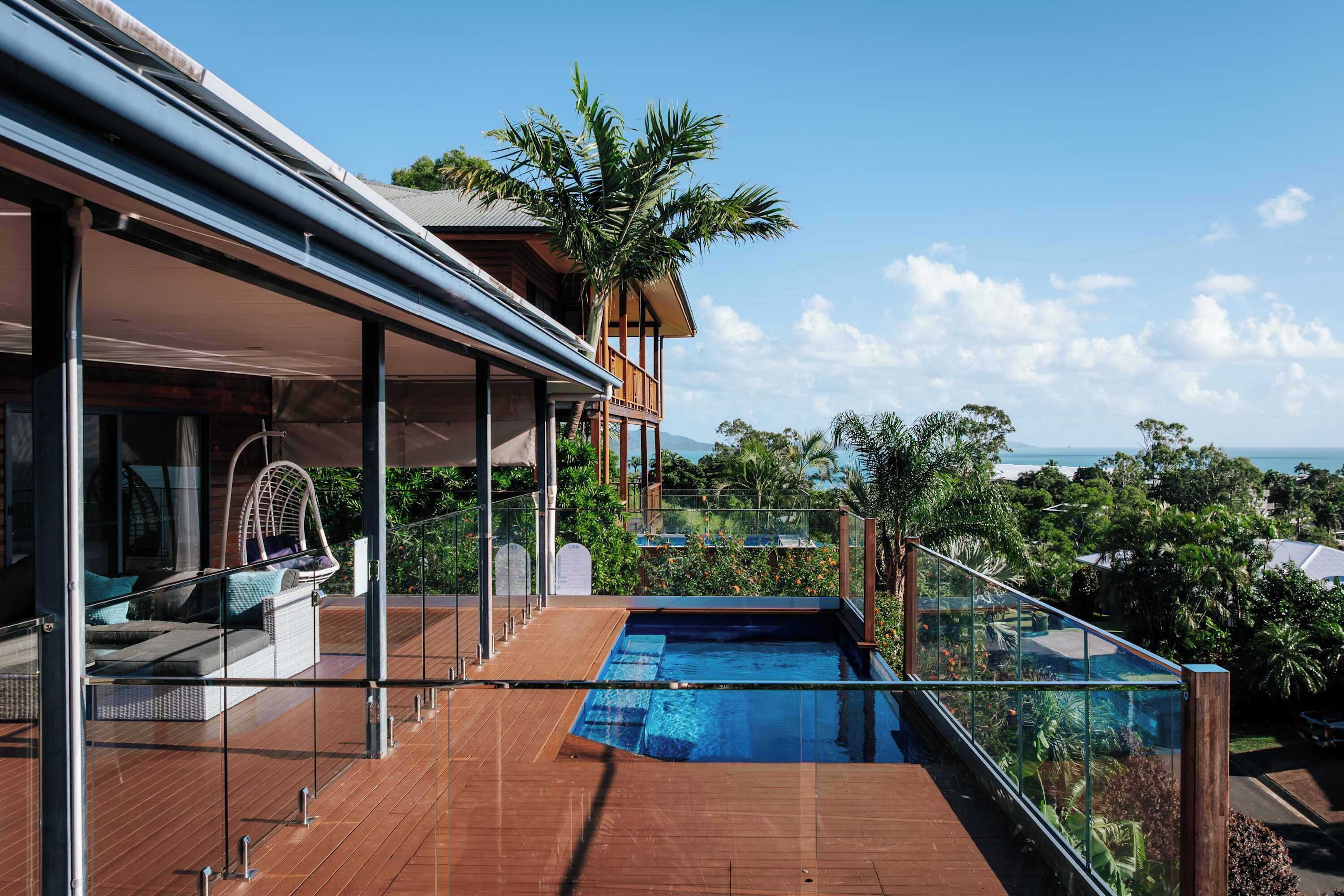 A modern house with a glass-enclosed swimming pool, a wooden deck, and a view of the ocean.