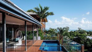 Ein modernes Haus mit einem überdachten Pool, einer Holzterrasse und Blick auf den Ozean.