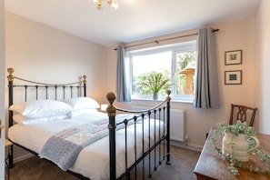 A bedroom with a bed, a window with curtains, a radiator, and a table with a plant.