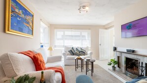 Ein Wohnzimmer mit einem weißen Sofa, einem blauen Sessel, einem Kamin und einem Bild an der Wand.