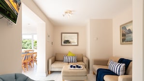 Ein Wohnzimmer mit Sofa, Hocker und Sessel, ein Essbereich mit Tisch und Stühlen sowie ein Bild an der Wand.