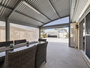 An outdoor patio with a covered seating area, a table, and a view of the backyard.