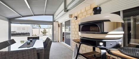 Un patio al aire libre con horno de pizza integrado, una mesa de comedor con sillas y una pared de ladrillo.