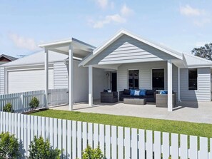 A modern two-story house with a covered patio, a fenced yard, and a well-maintained lawn.