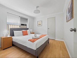 A bedroom with a bed, nightstands, a window with blinds, a door, and a ceiling light.