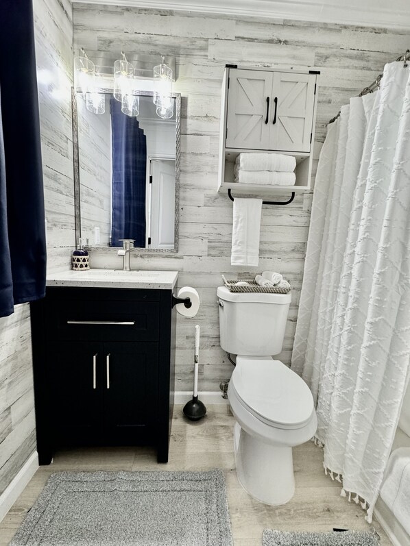 Et moderne badeværelse med et hvidt toilet, en sort kommode og et spejl.
