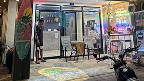 A storefront with a neon sign, outdoor seating, and a scooter parked in front. - Broccoli candy hotels  (Karon)