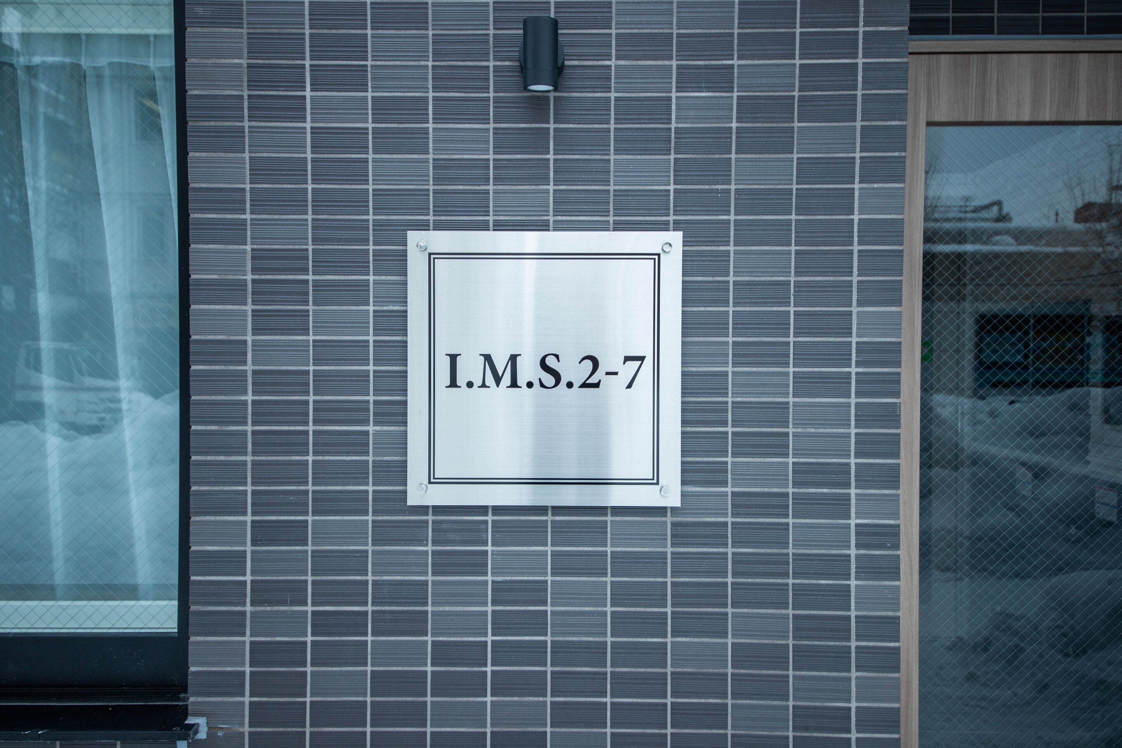 Un letrero con el texto 'I.M.S. 2-7' montado en una pared con azulejos.
