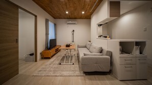 A modern living room with a wooden ceiling, a grey sofa, a wooden coffee table, and a white cabinet. - Astral 103 (Asahikawa)