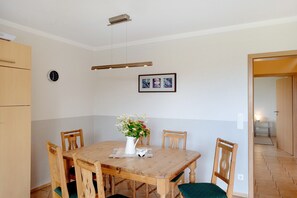 Ein Essbereich mit einem Holztisch, Stühlen, einer Blumenvase, einer Uhr und gerahmten Bildern an der Wand.