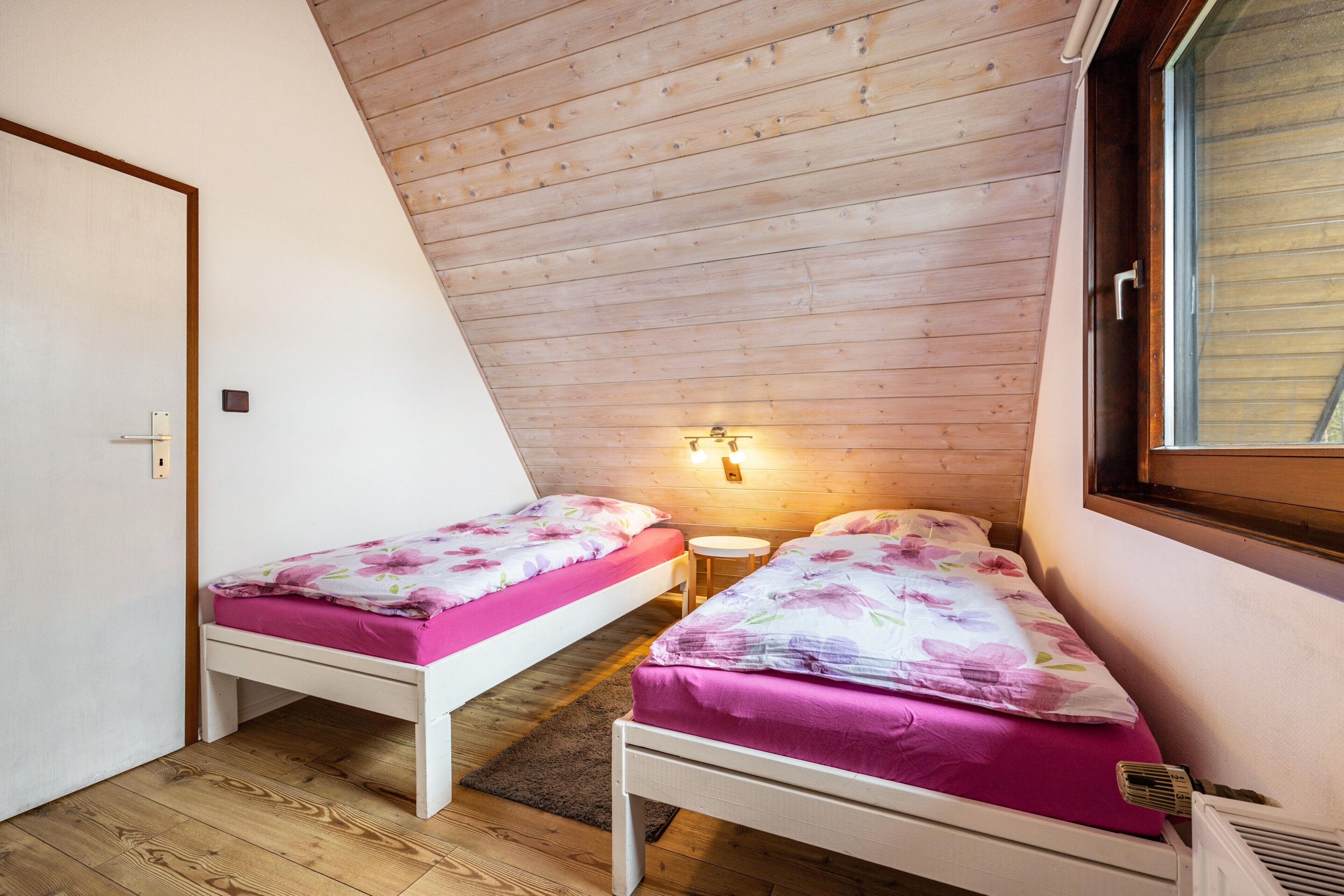 A small, single-room accommodation with two beds, wooden ceiling, and a window.