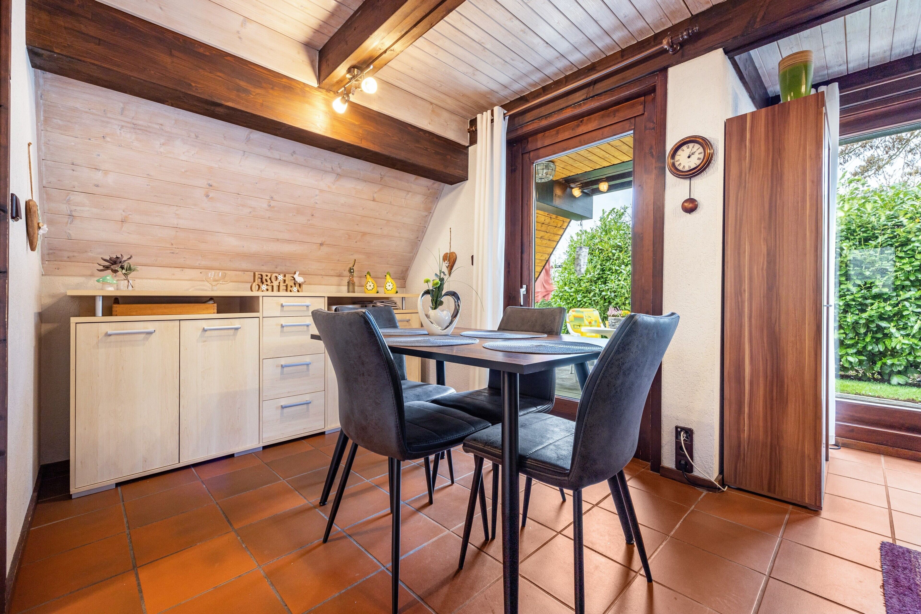 Cocina con mesa y sillas, armarios de madera y ventana con vistas al verdor.