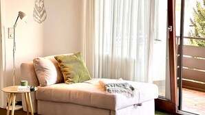 A modern living room with a sofa, a small table, a lamp, and a view through a glass door.