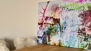 A wooden dining table with white furry chairs, a fluffy rug, and a colorful abstract painting on the wall.