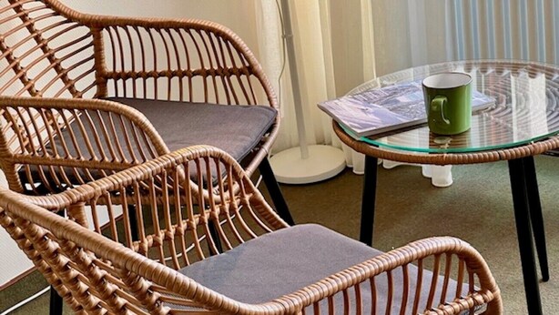 Wicker chairs with cushions, a glass table, and a green mug.