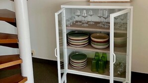 A staircase with wooden steps and a white column, a framed picture of an elk, and a glass cabinet with plates and glasses.