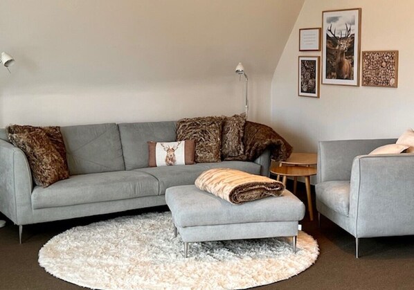 Un soggiorno moderno con un divano grigio, un pouf abbinato, un tappeto rotondo bianco e un piccolo tavolino in legno.