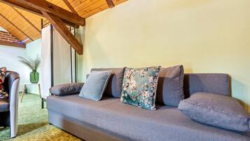 Un sofá gris con cojines florales y grises lisos, techo de madera y vistas a una habitación con una silla y un florero.