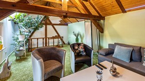 Una habitación con techo de madera alto, un sofá, una silla, una mesa y una escalera que lleva a otro nivel.