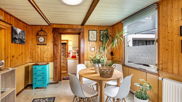 Una habitación con paneles de madera, una mesa de comedor, sillas, un aparador azul y un ventanal con vistas.