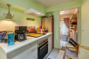 Une cuisine compacte équipée d’une machine à café, d’une bouilloire et d’une planche à découper en bois.