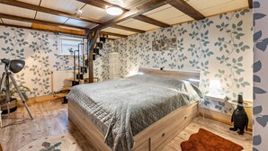 Un dormitorio con una cama grande, vigas de madera, un radiador, un escritorio, una lámpara y una planta pequeña.
