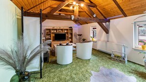 Un loft espacioso con techos altos, vigas de madera a la vista, un televisor de pantalla plana grande y una zona de estar acogedora con otomanas.