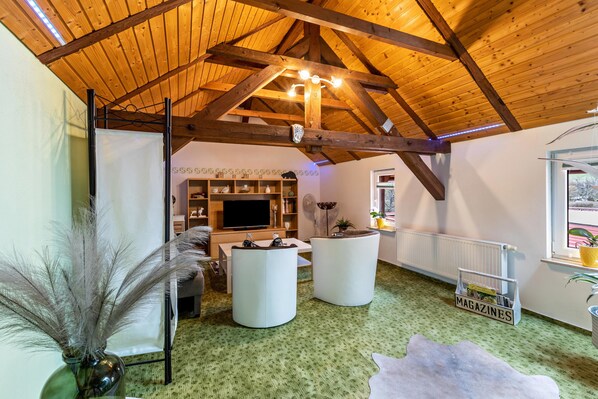 Un loft spacieux avec de hauts plafonds, des poutres apparentes, un grand téléviseur à écran plat et un coin salon confortable agrémenté de poufs.