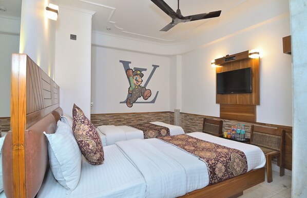 A hotel room with a large bed, a ceiling fan, a TV mounted on the wall, and a decorative wall piece.