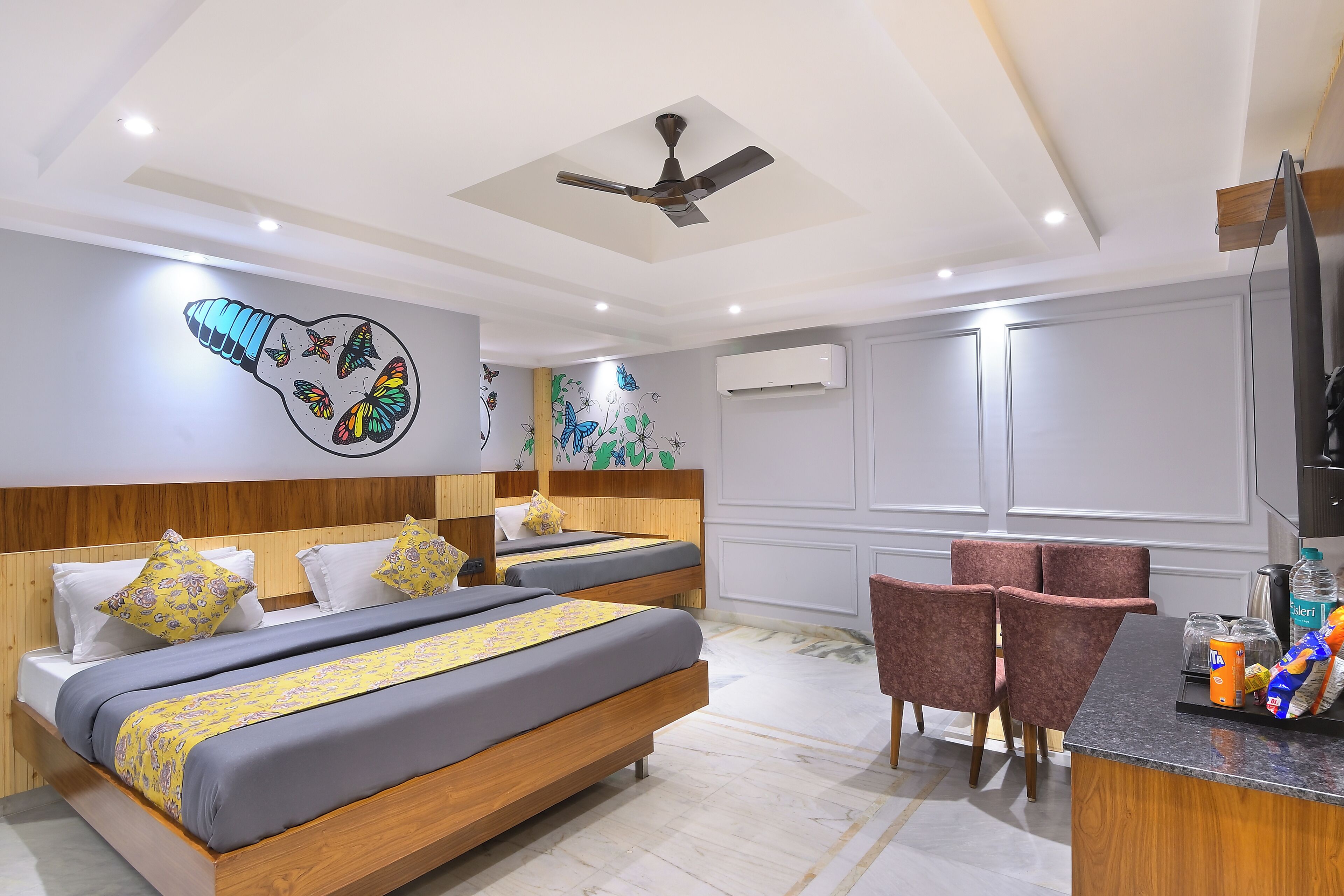 A hotel room with two beds, a ceiling fan, a small kitchen area, and a seating area with chairs.