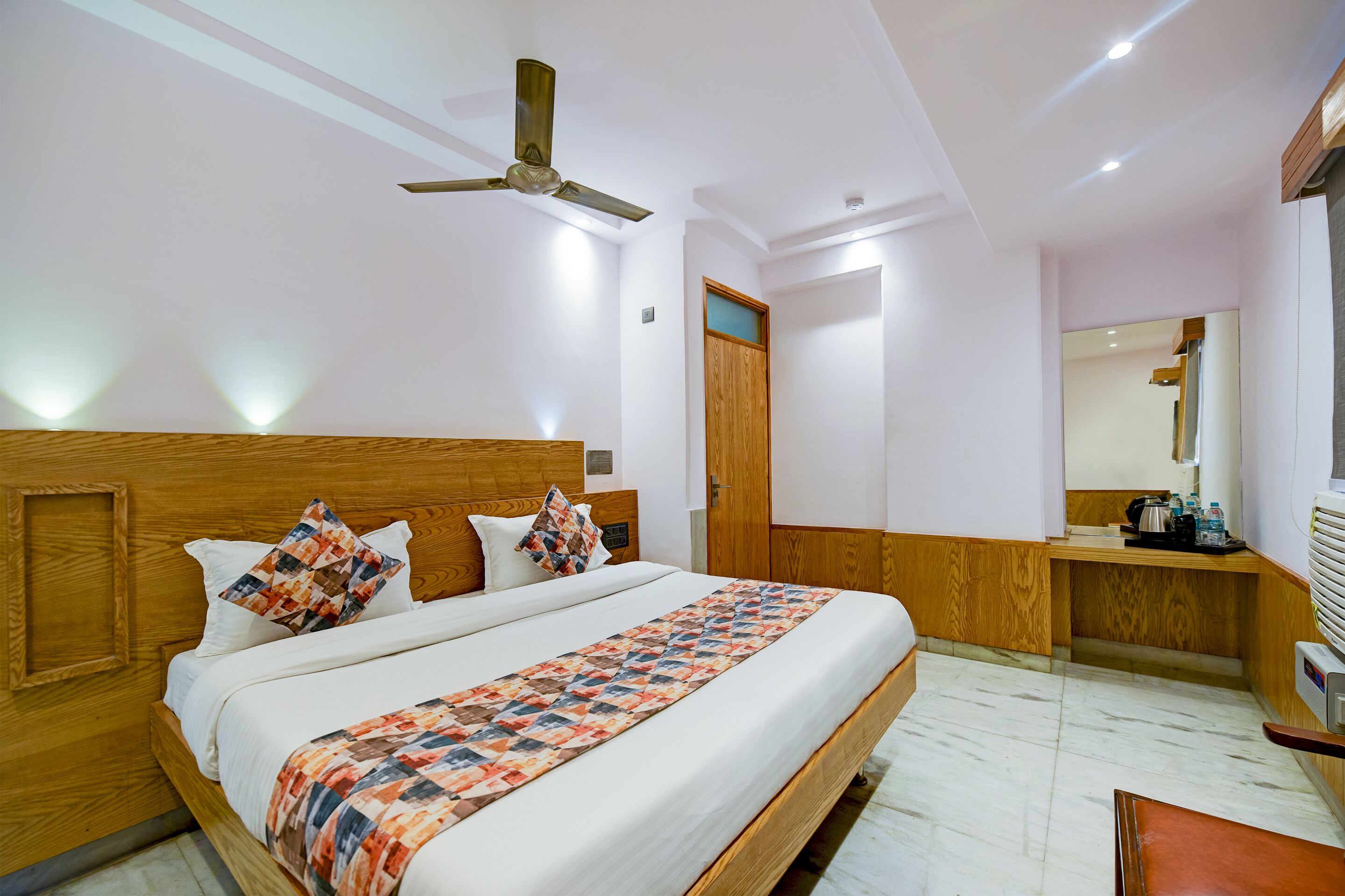 A bedroom with a wooden bed, a ceiling fan, a bedside table, and a mirror.