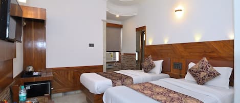 Une chambre d’hôtel avec deux lits, une télévision, un bureau avec des collations, un ventilateur de plafond et une salle de bain visible à travers une porte ouverte.