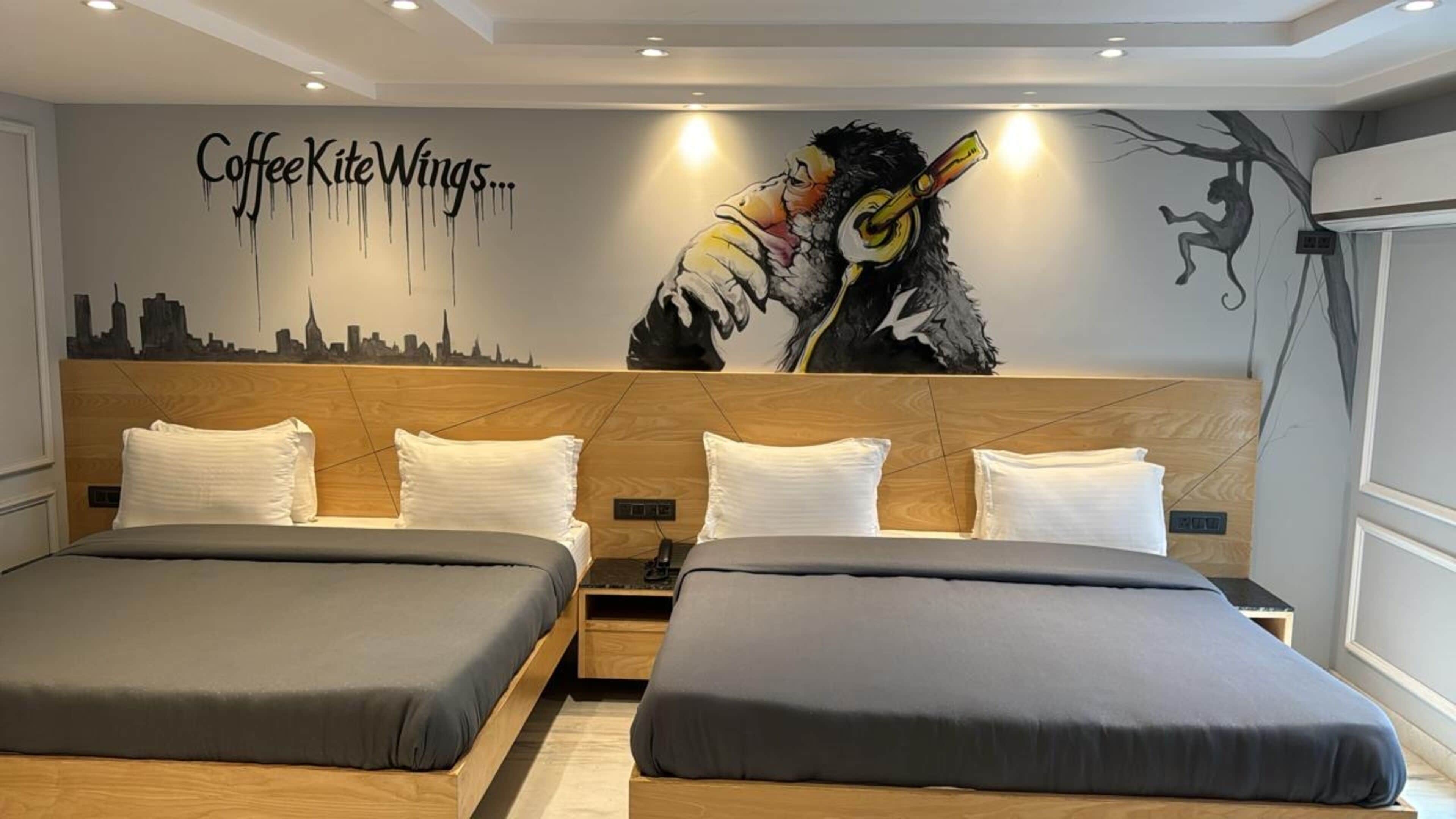 A hotel room with two beds, a city skyline mural, and a large artwork of a person with wings.