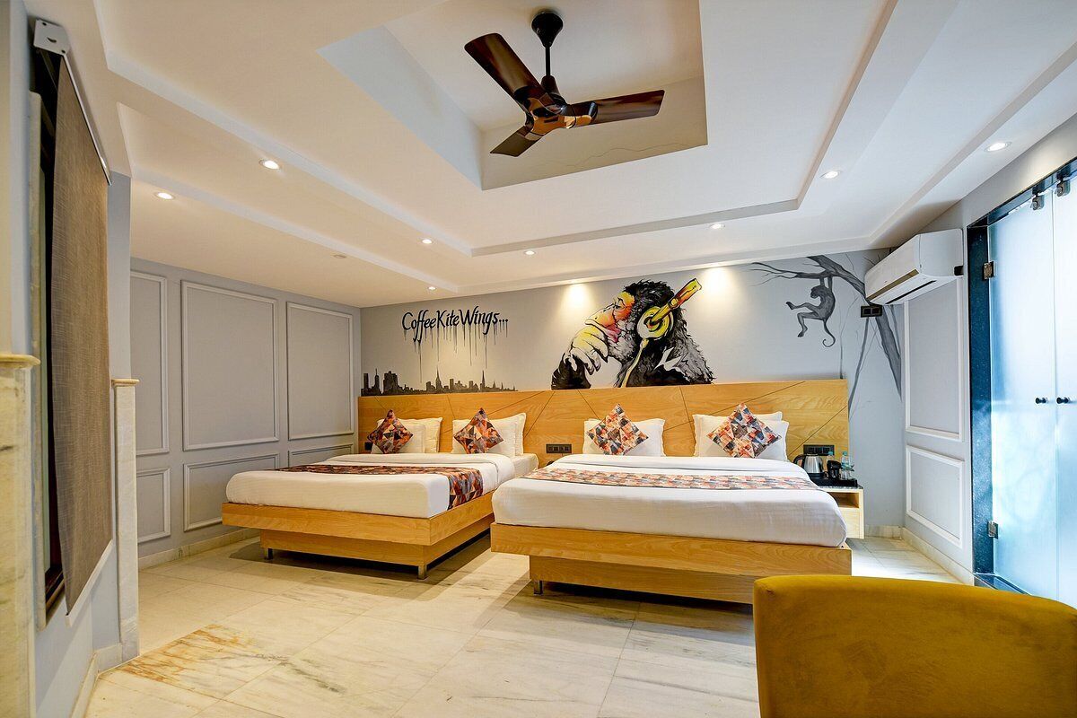 Habitación de hotel moderna con dos camas, ventilador de techo, un mural y vistas a la línea del horizonte de la ciudad.