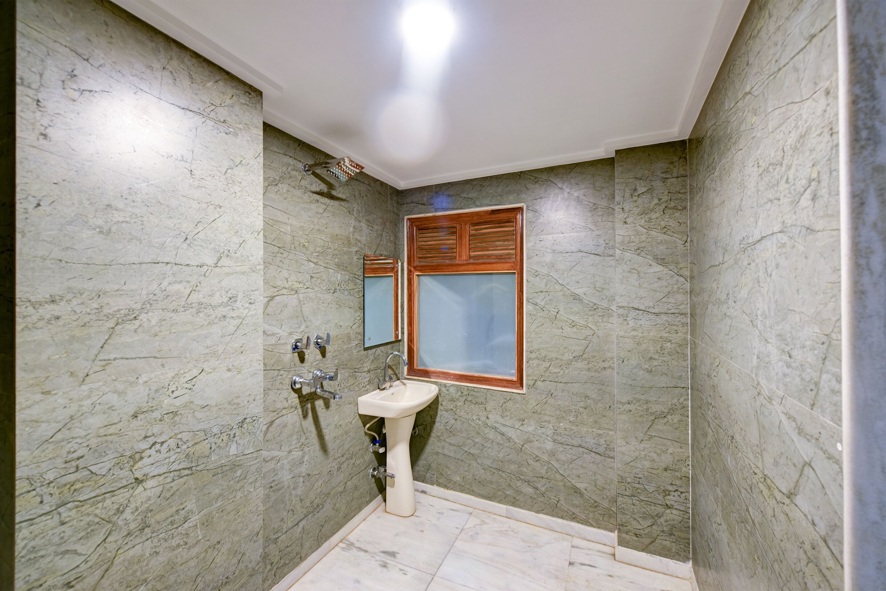 A bathroom with a marble wall, a pedestal sink, and a mirror with a wooden frame.