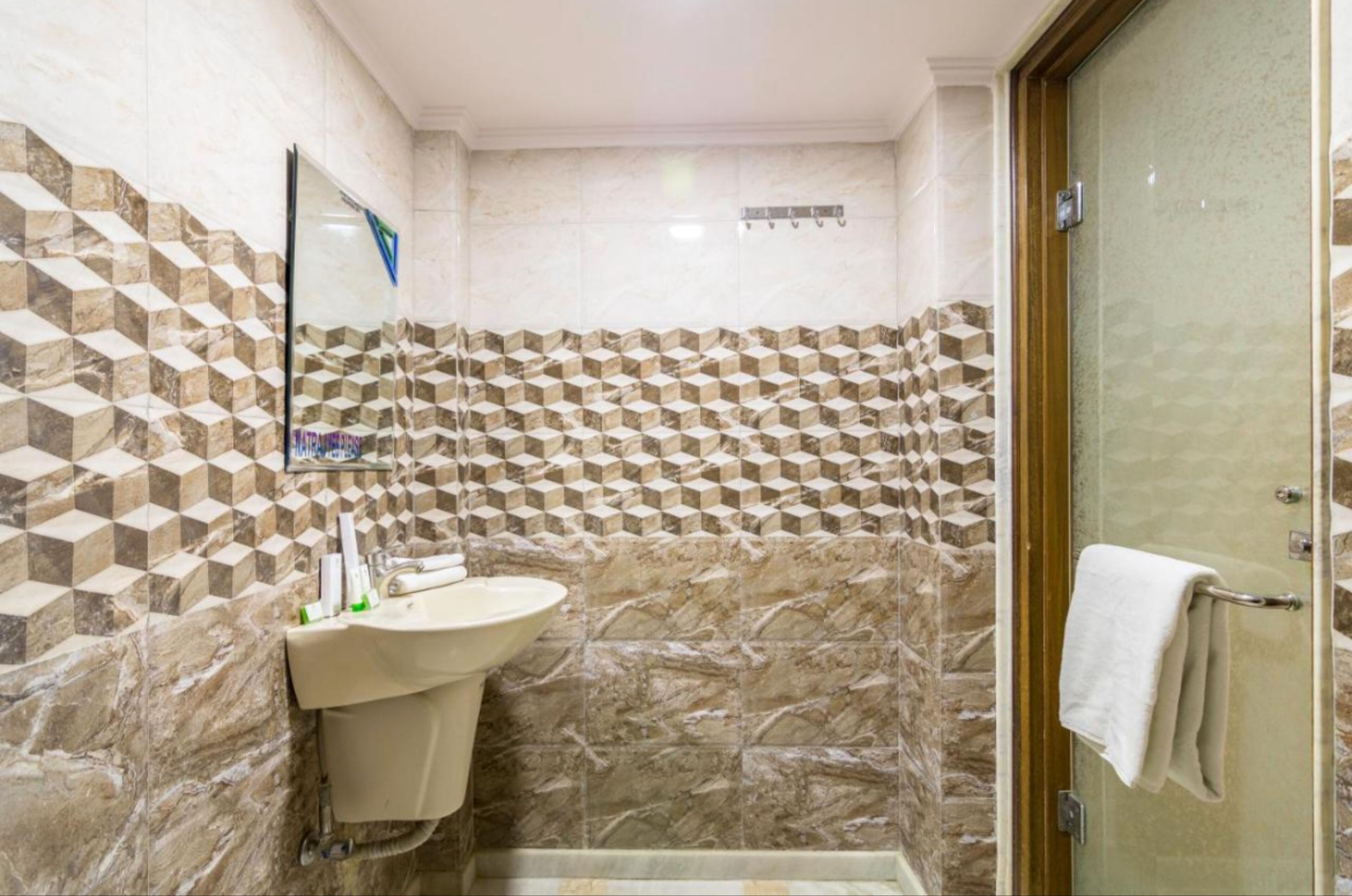 Un baño con pared de azulejos de diseño geométrico, un lavabo y una cabina de ducha de cristal.