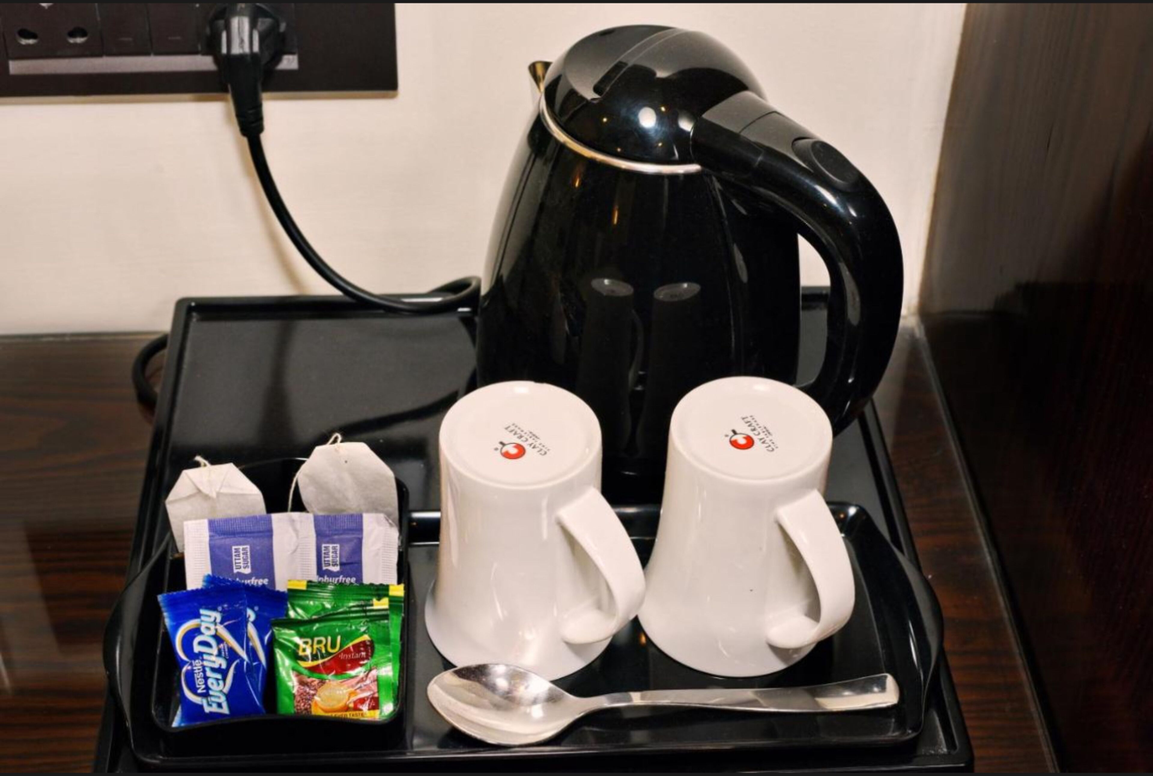 Una cafetera, dos tazas blancas, una cuchara y algunos paquetes de comida sobre una bandeja.