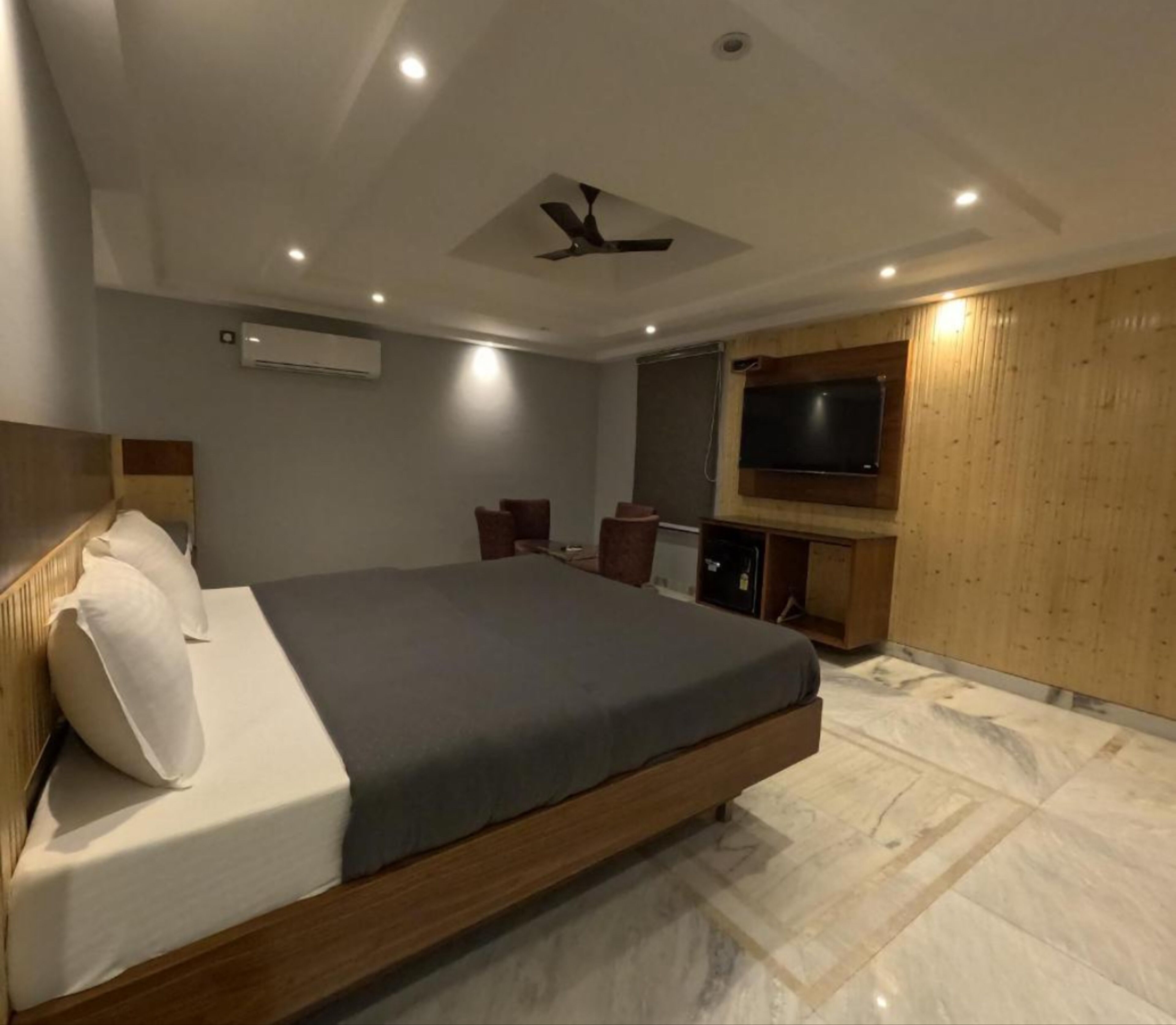 A modern bedroom with a large bed, a ceiling fan, a TV, and a wooden panel wall.