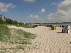 Ein Strand mit Sand, Gras und Holzgebäuden.
