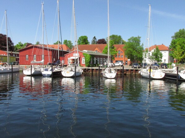 Un port de plaisance où sont amarrés plusieurs voiliers, des bâtiments aux façades rouges et blanches, et une surface d’eau calme qui reflète les bateaux.