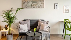A living room with a sofa, a round coffee table, a potted plant, and a painting on the wall.