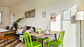 A modern living room with a sofa, a dining table with chairs, a lamp, and wall art.