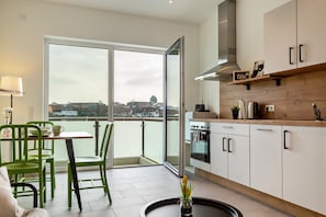 A modern kitchen with a large window, a dining area with green chairs, and a view of a cityscape. - Apartment Mina in Geratskirchen – Quiet, Cozy, and Close to Nature (Geratskirchen)